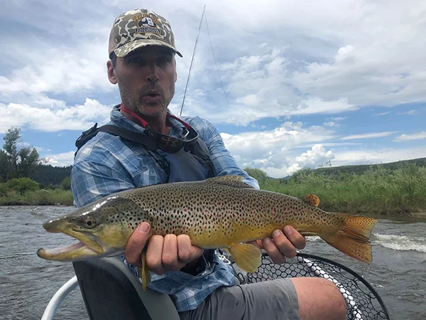 A man holding a brown fish while sitting on a boat.