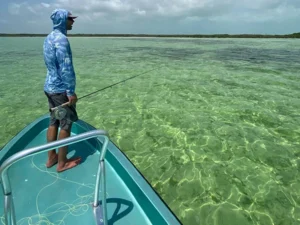 A man standing on the bow of a boat in shallow water.