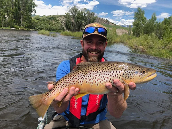 A man holding a brown fish while sitting in the water.