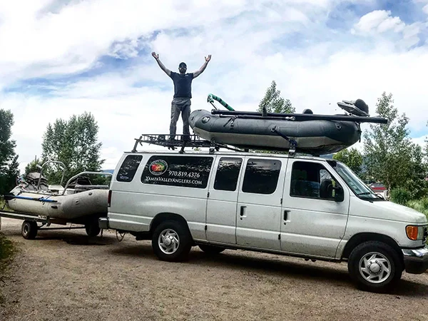 A man standing on the back of a van with a boat on top.