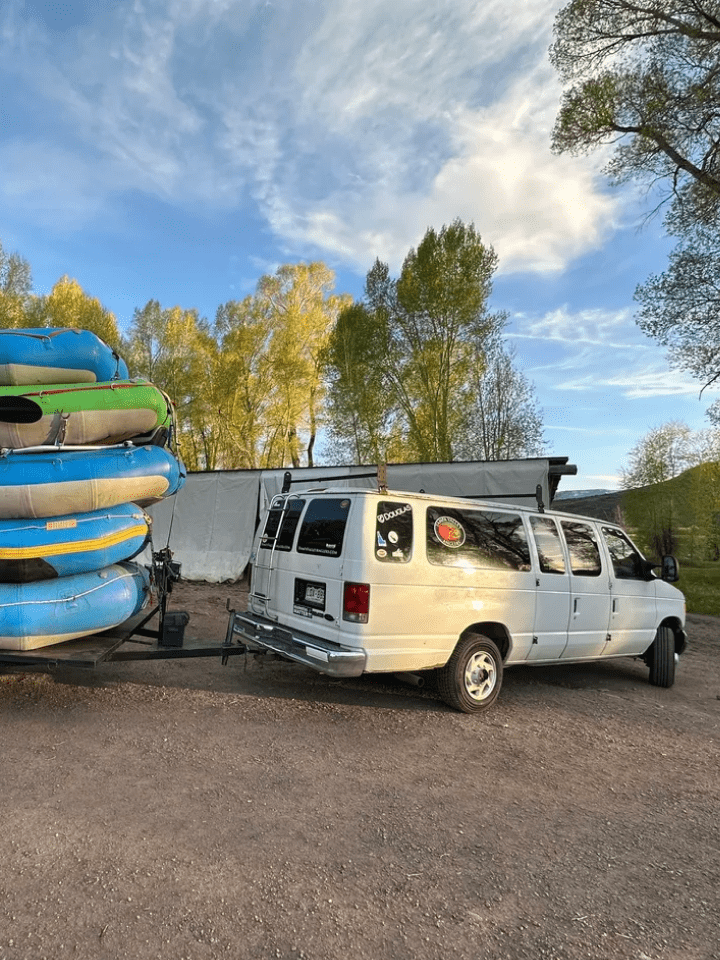 A van parked next to a trailer with several boats.