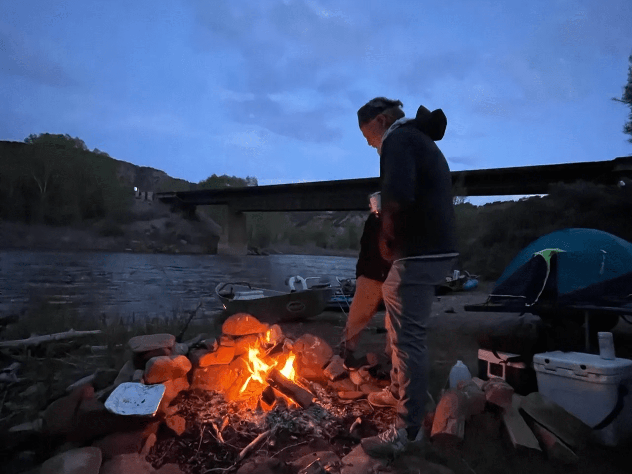 A man standing next to a fire in the middle of nowhere.