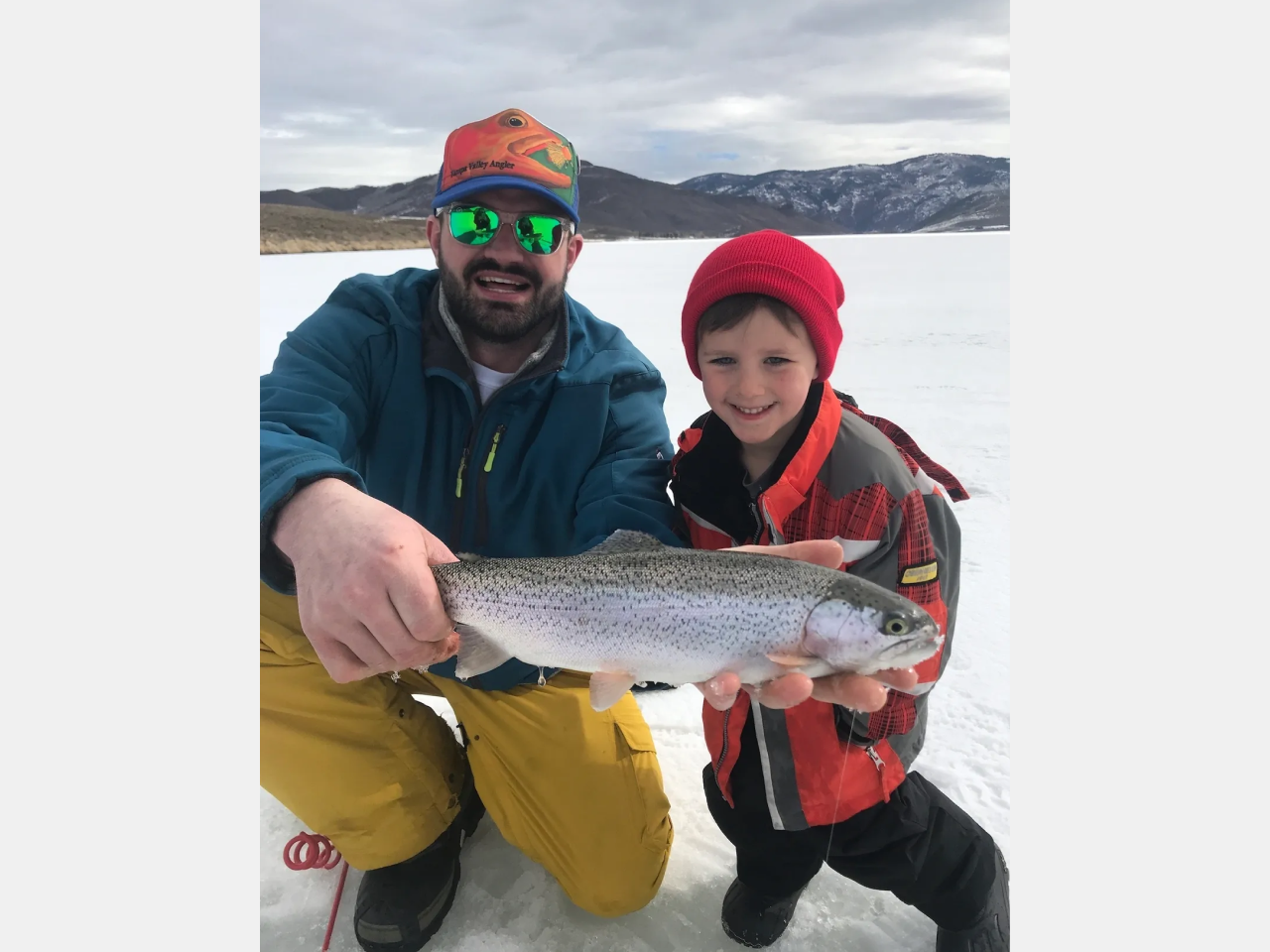 A man and boy holding a fish in the snow.