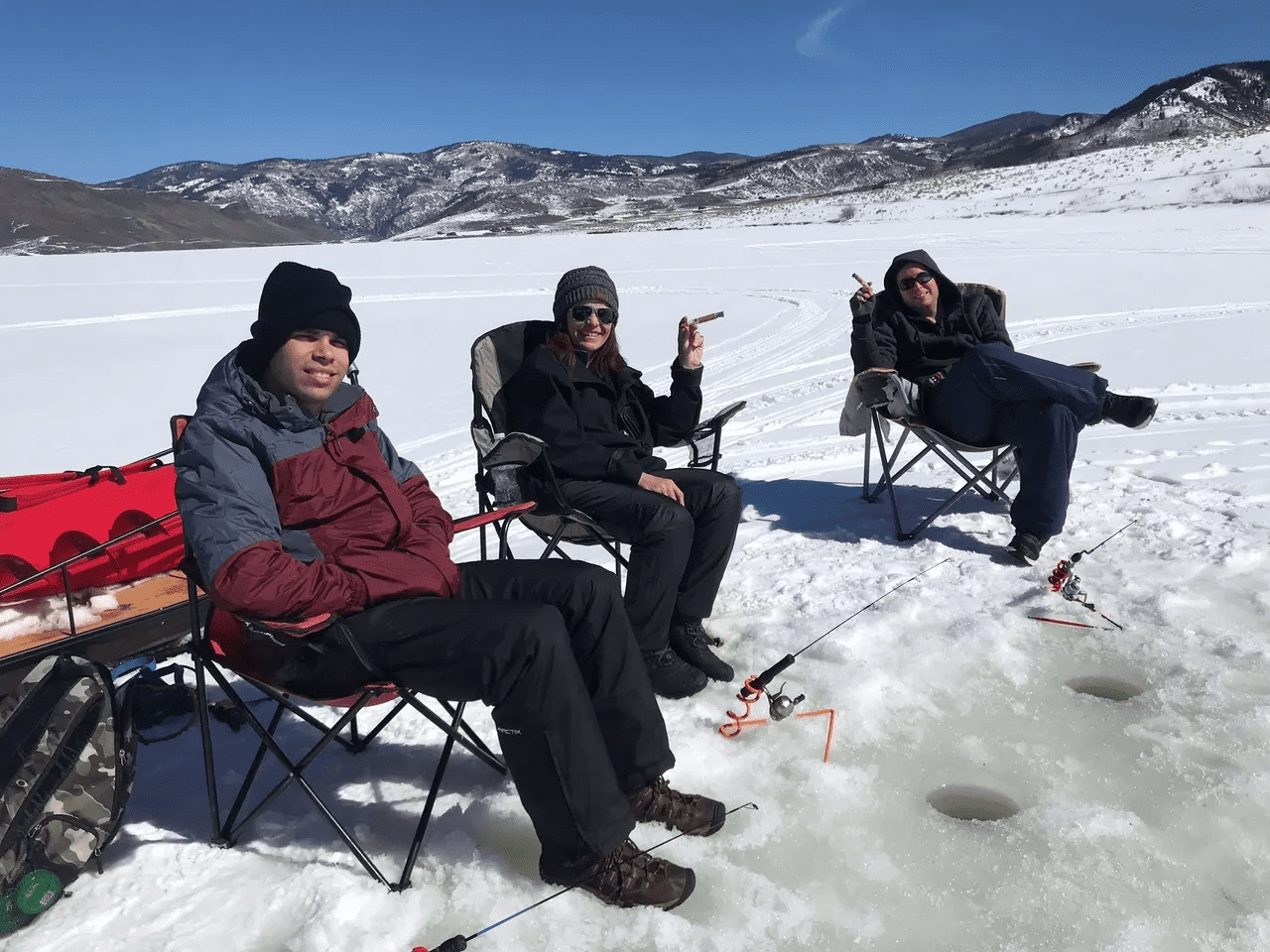 Three people sitting in folding chairs on a snowy hill.