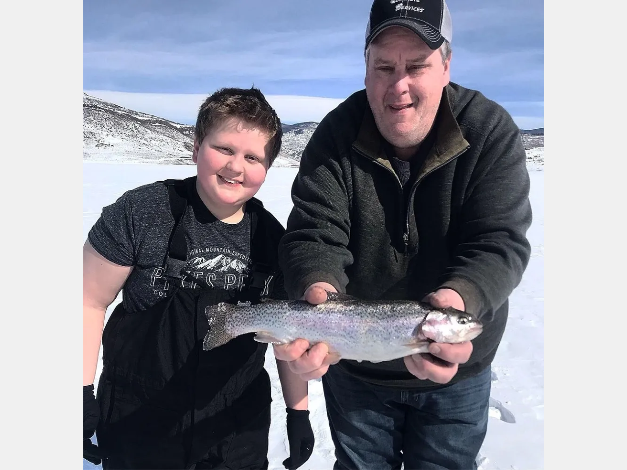 A man and boy holding a fish in the snow.