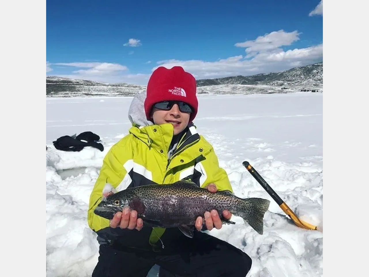 A boy holding a fish in his hands while sitting on the snow.