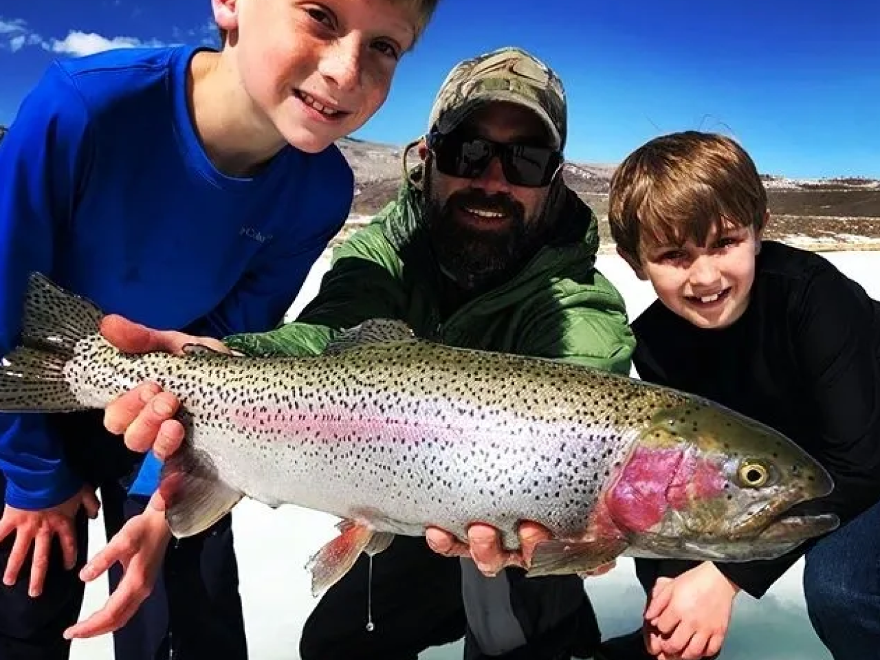 A group of people holding a rainbow trout.