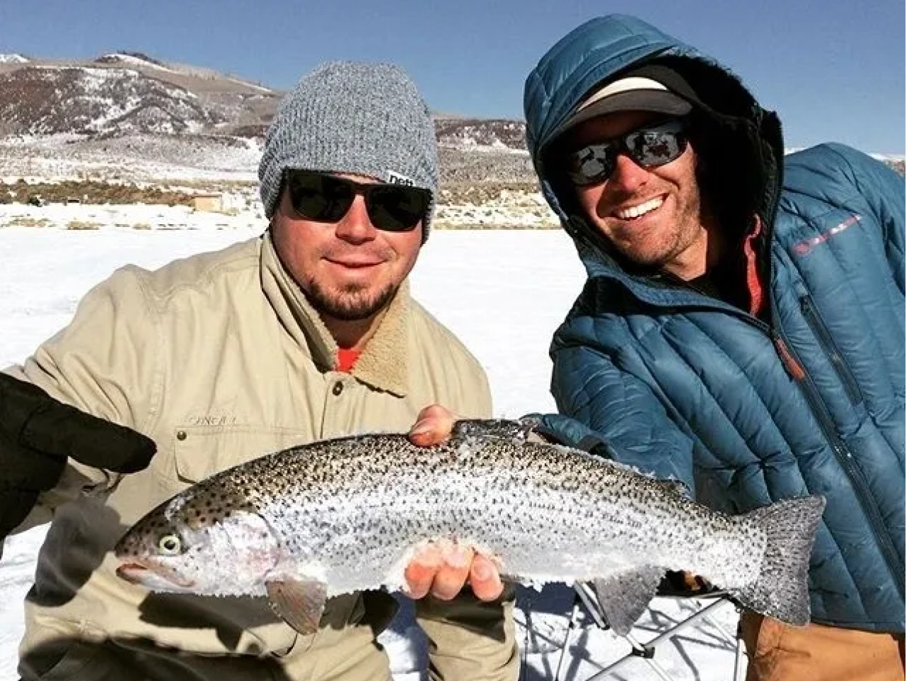 Two men holding a fish while standing on snow covered ground.