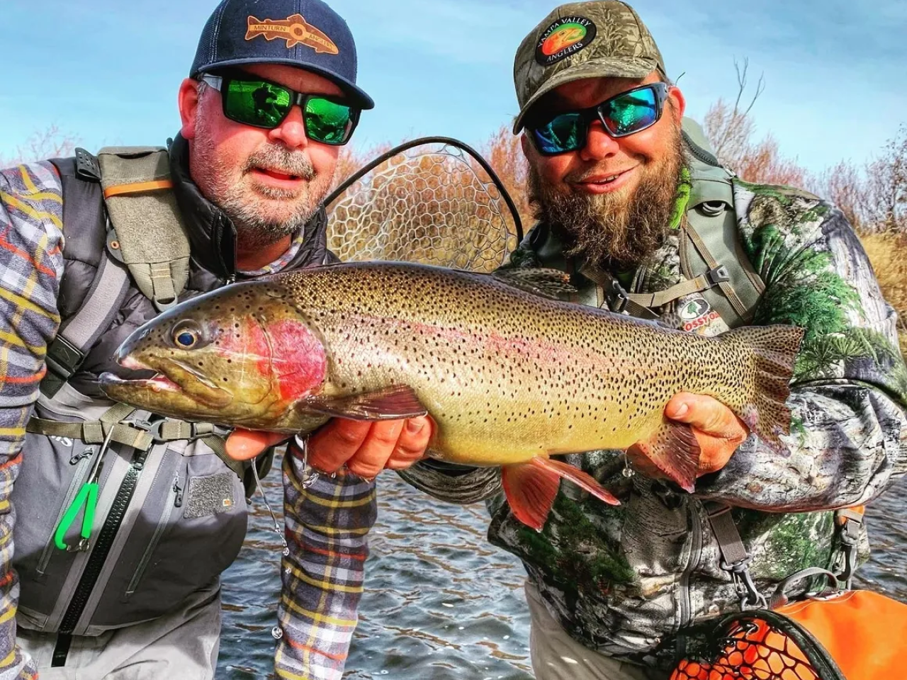 Two men holding a fish while standing on the shore.