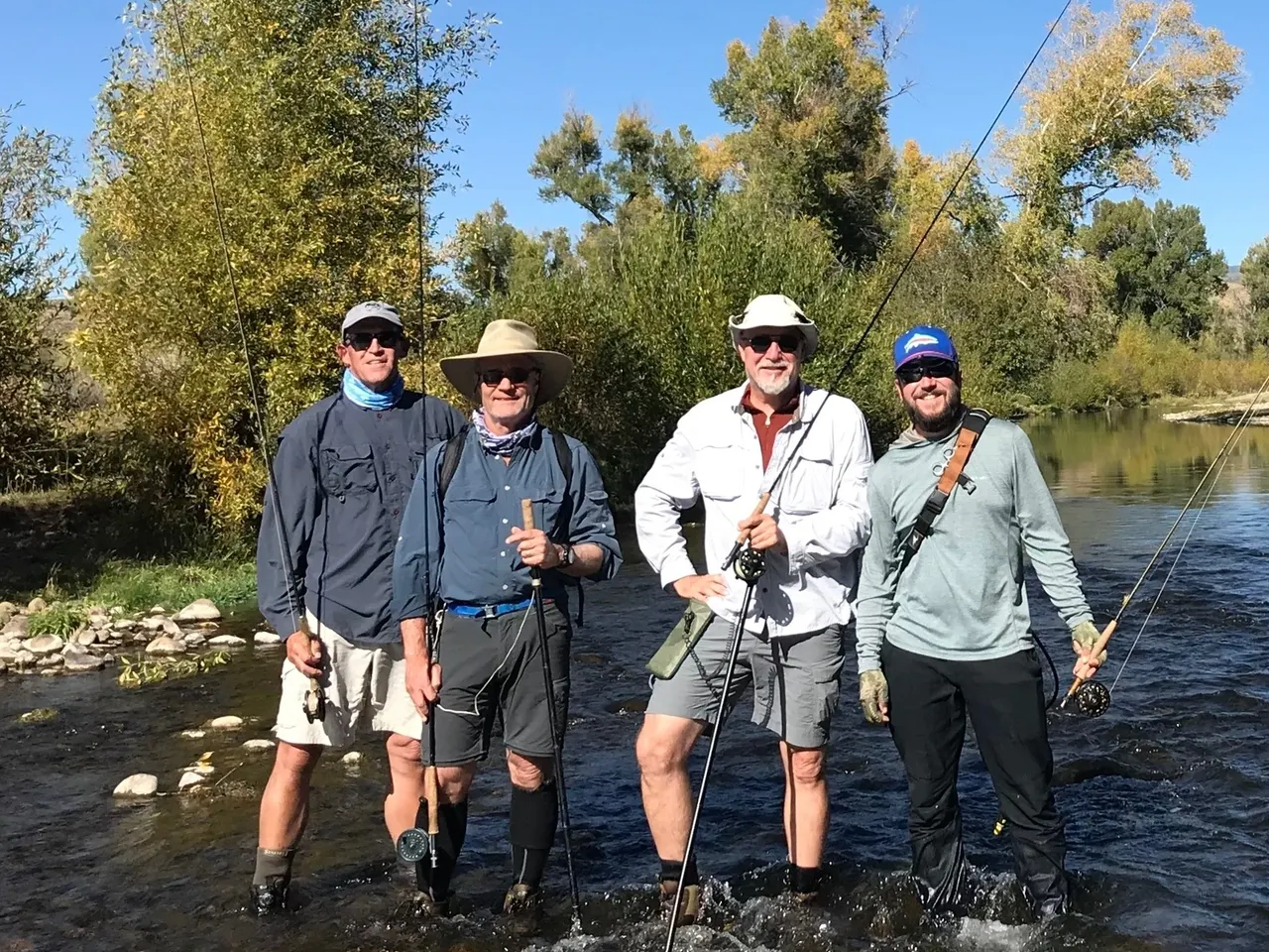 Four men standing in a river holding fishing rods.