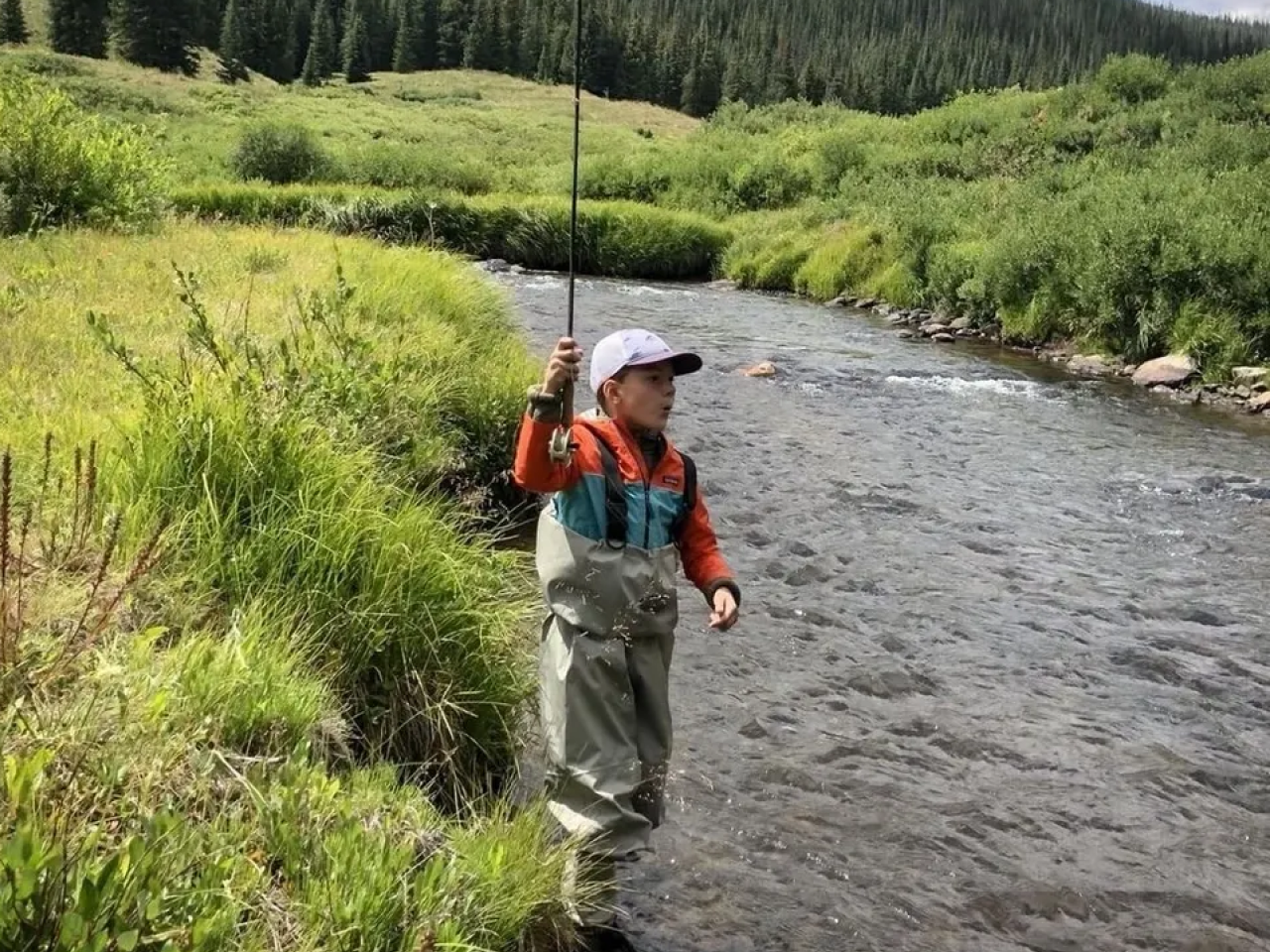 A man standing in the middle of a river holding a fishing pole.