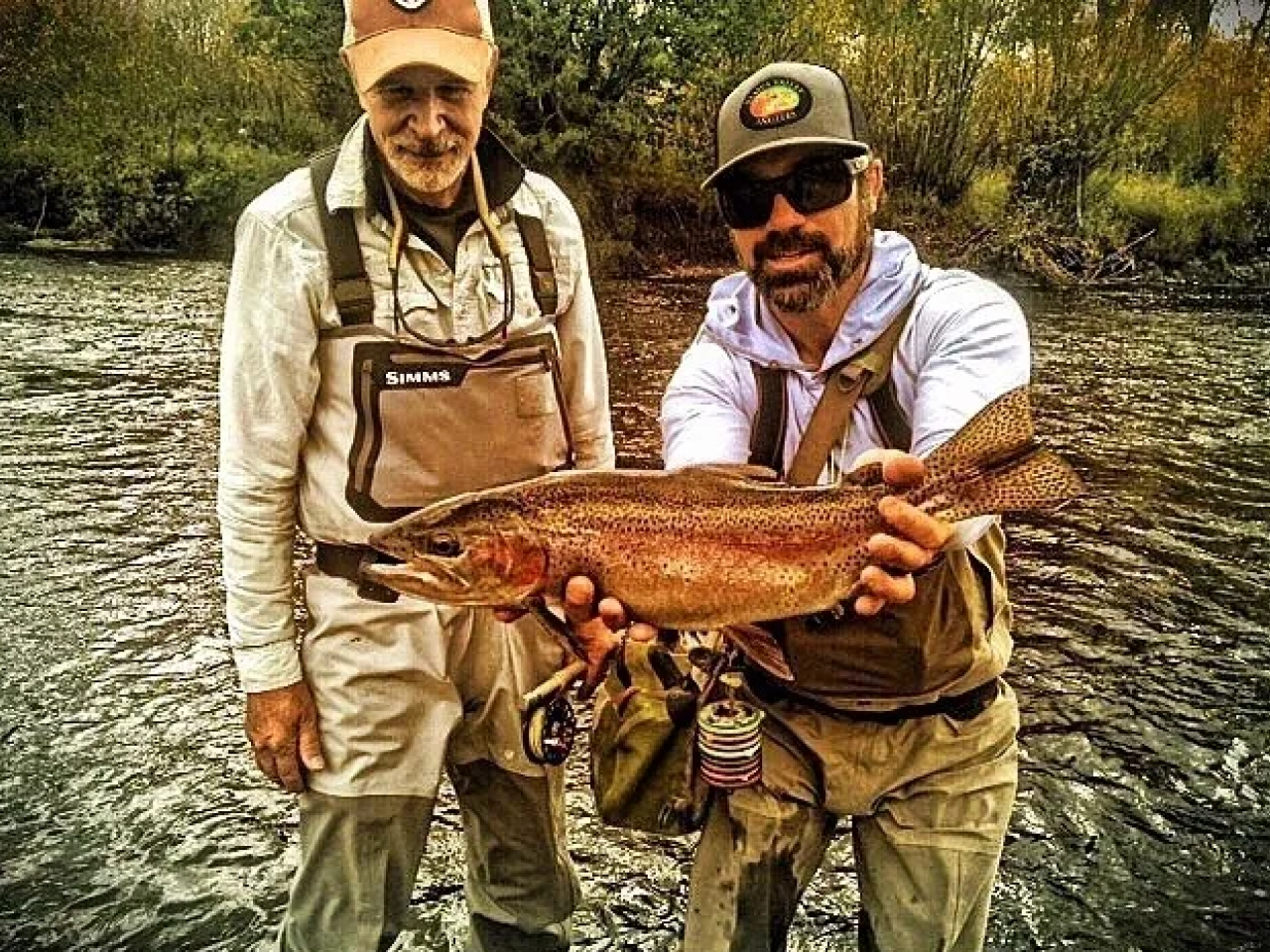 Two men holding a fish in the water.