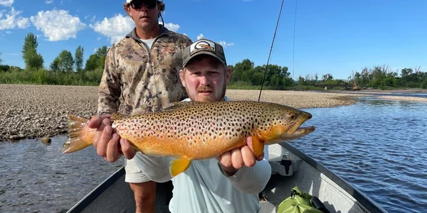 A man holding a brown fish while standing on top of a boat.