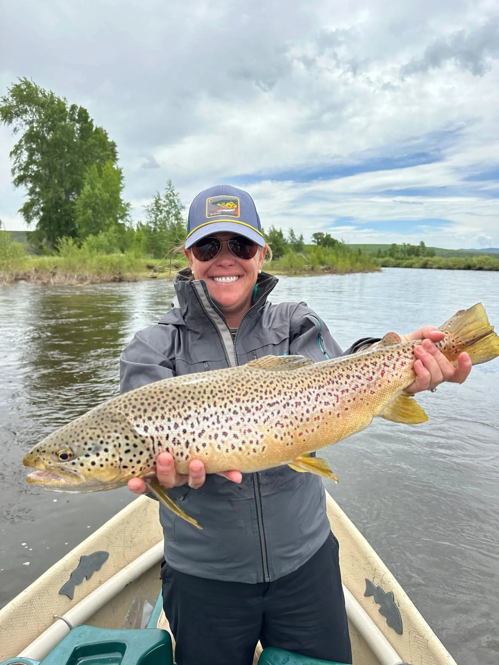 A woman holding a brown fish while standing on top of a boat.