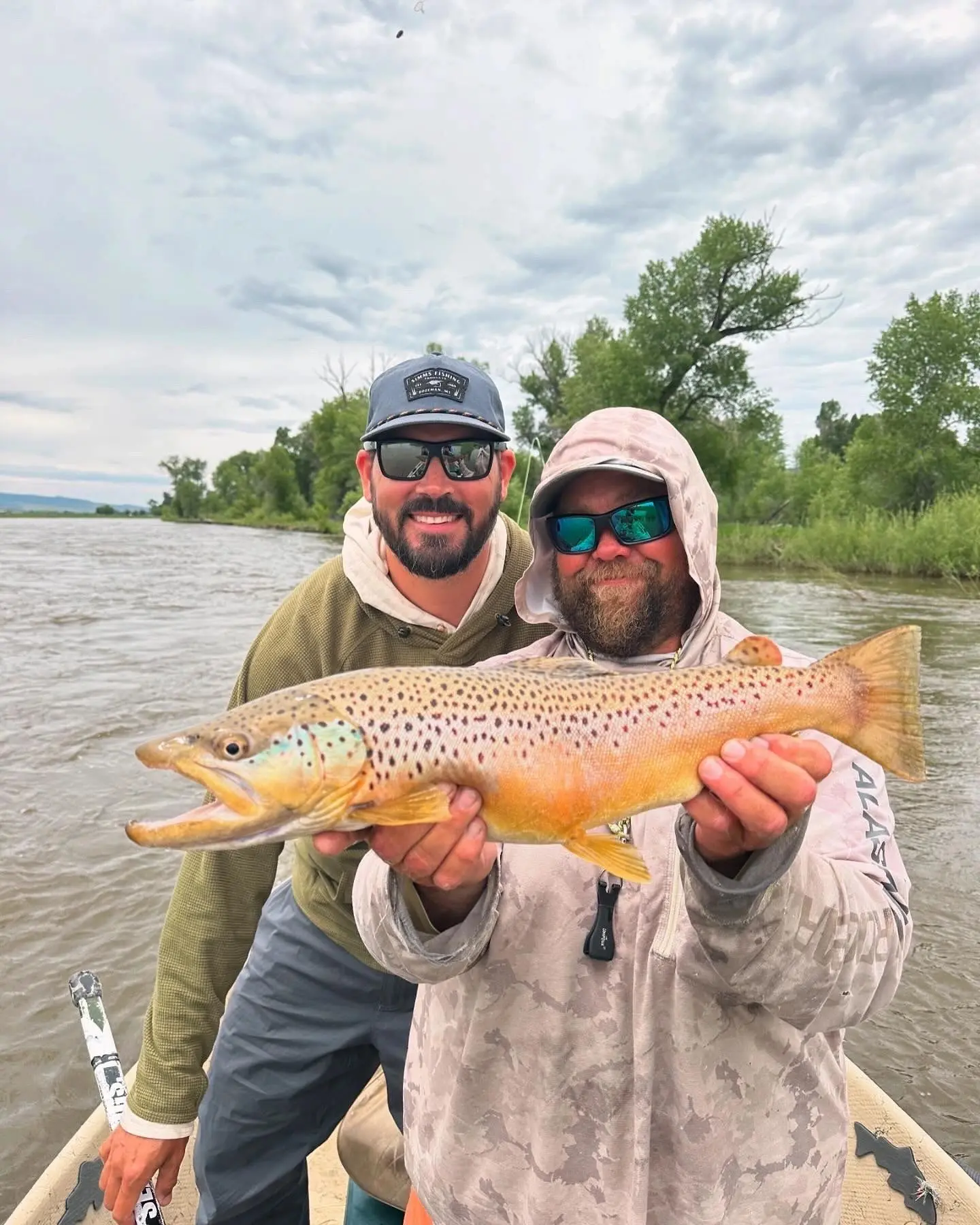 Two men holding a brown fish while standing on the water.