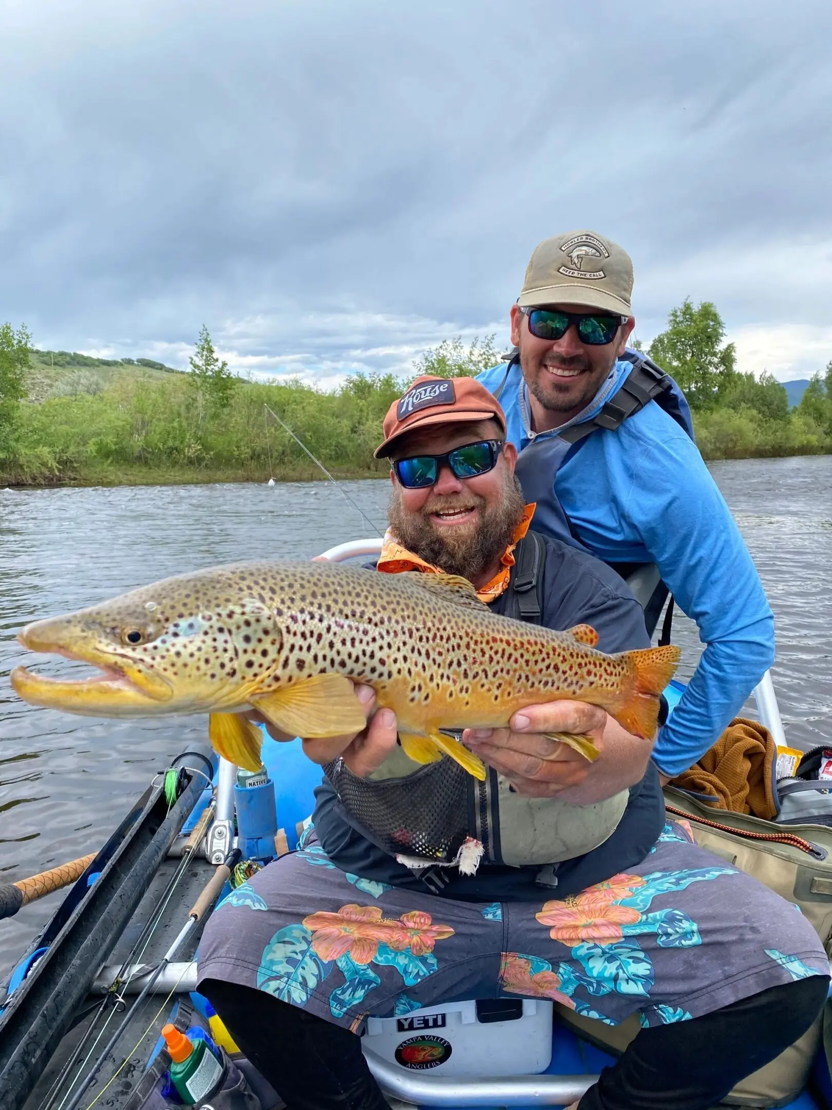 Two men holding a brown fish while standing on a boat.