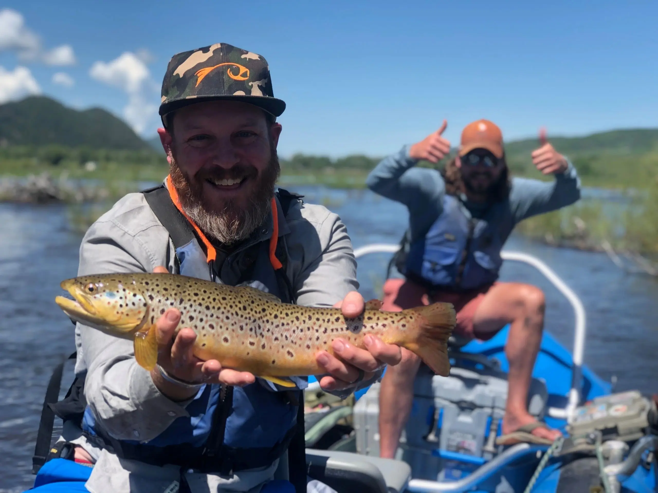 Two men holding a brown fish on top of a boat.