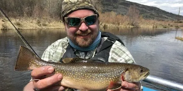 A man holding a fish while wearing sunglasses.