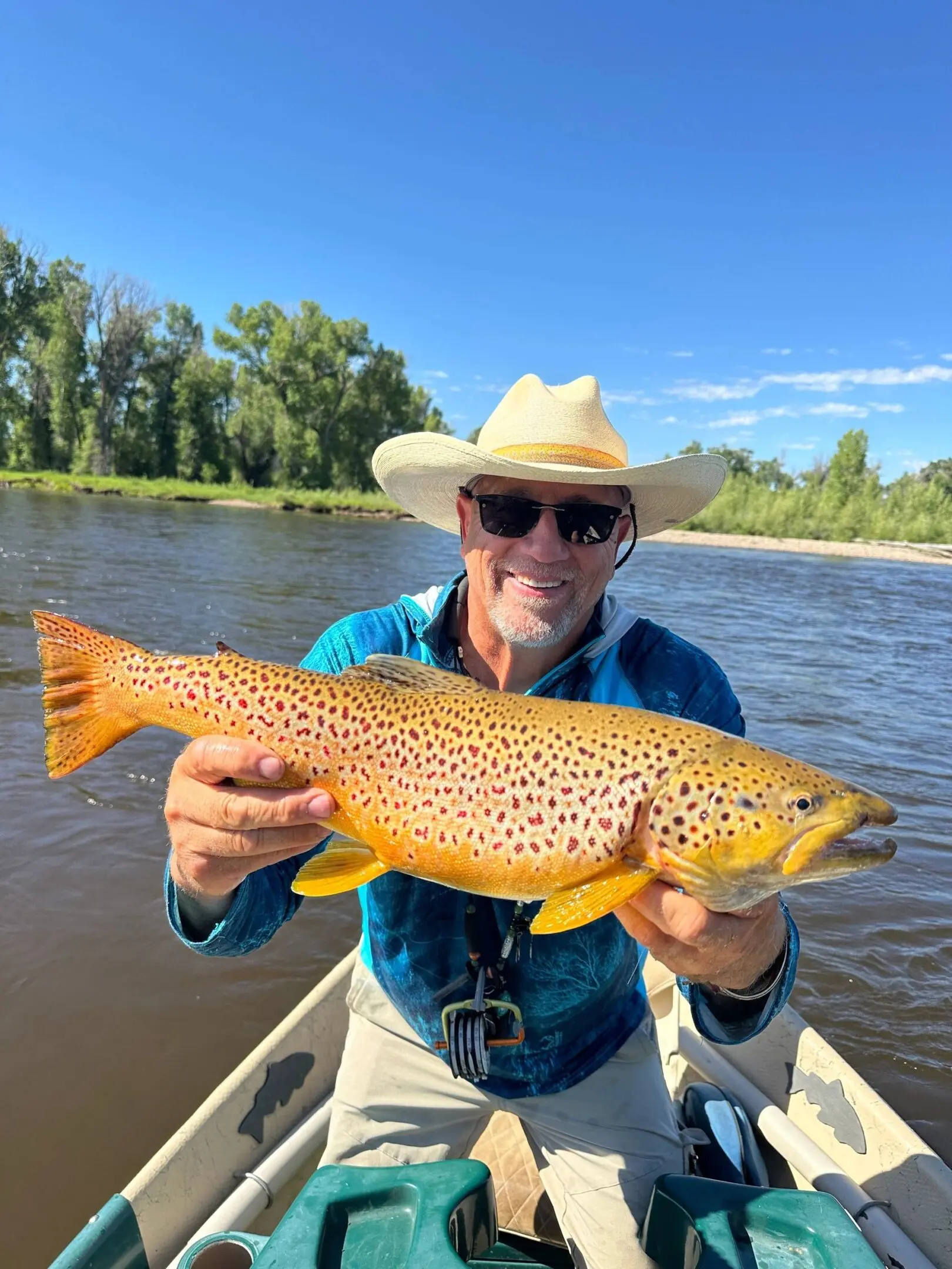 A man holding a brown fish while standing on top of a boat.