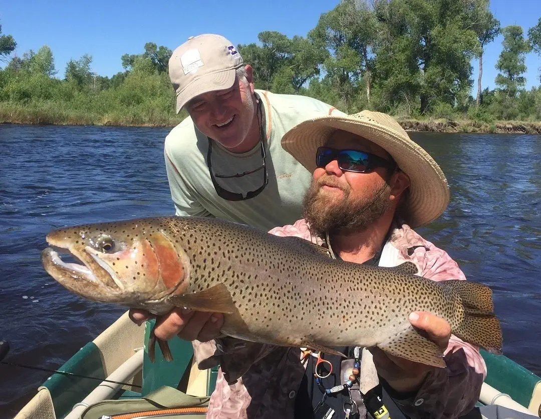 Two men holding a large fish on the water.