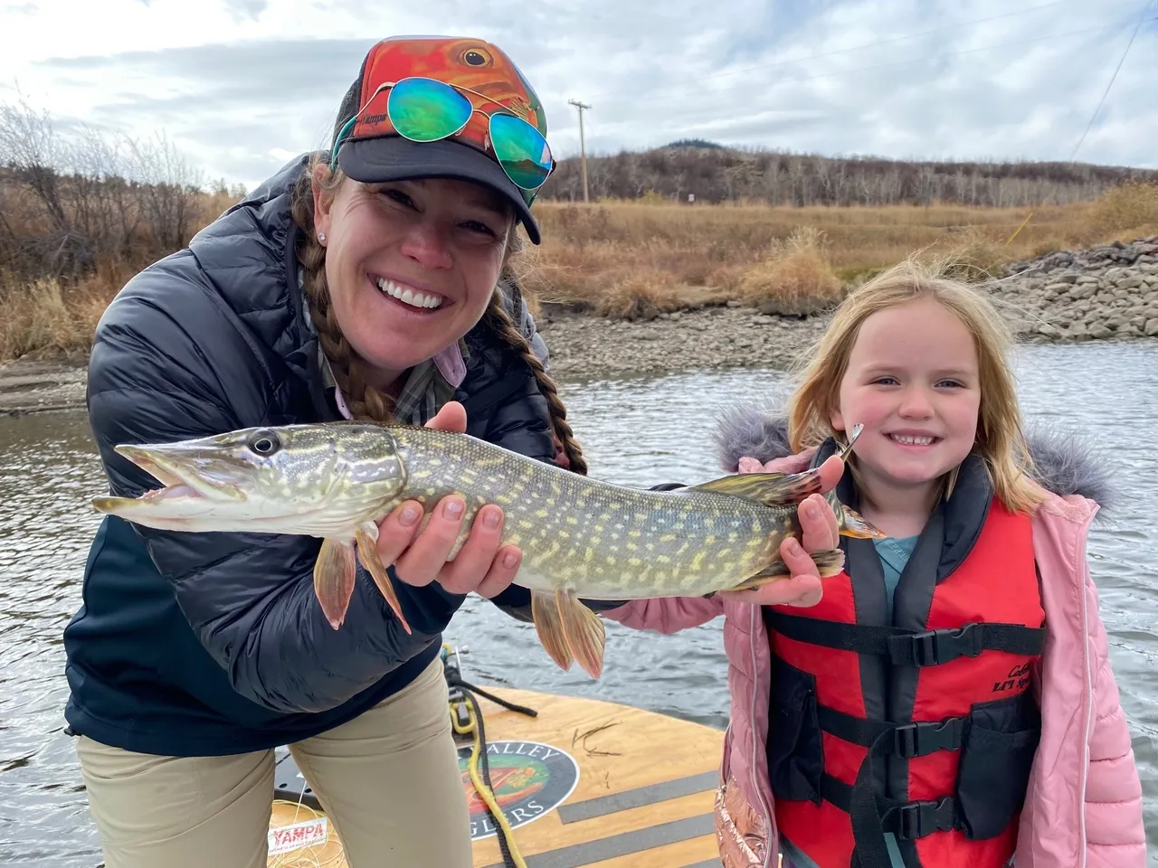 A woman and girl holding a pike fish.