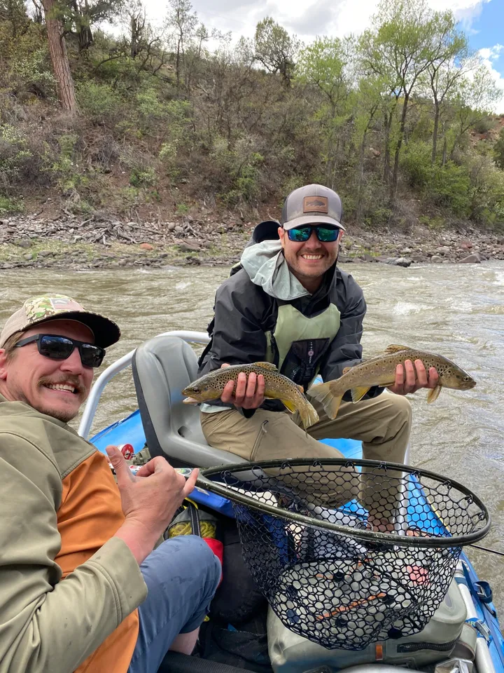 Two men are holding fish while sitting on a boat.