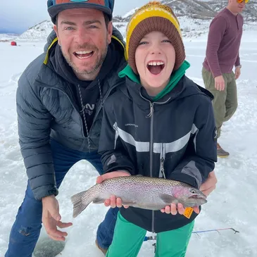 A man and boy holding a fish in the snow.