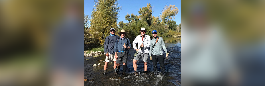 Four people standing in a river holding fishing rods.