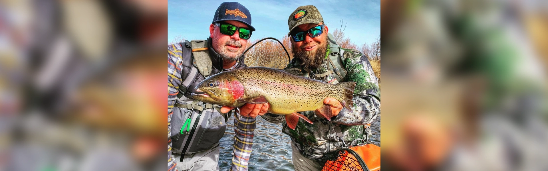 Two men holding a fish while standing in the water.