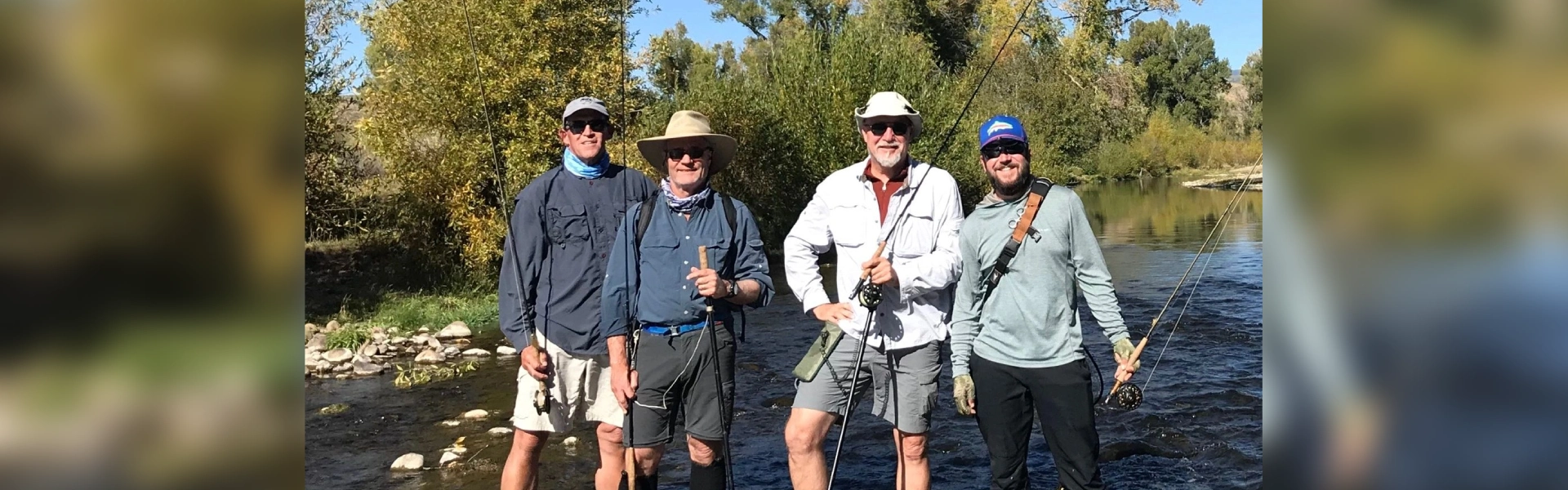 A group of men standing in the water holding fishing rods.