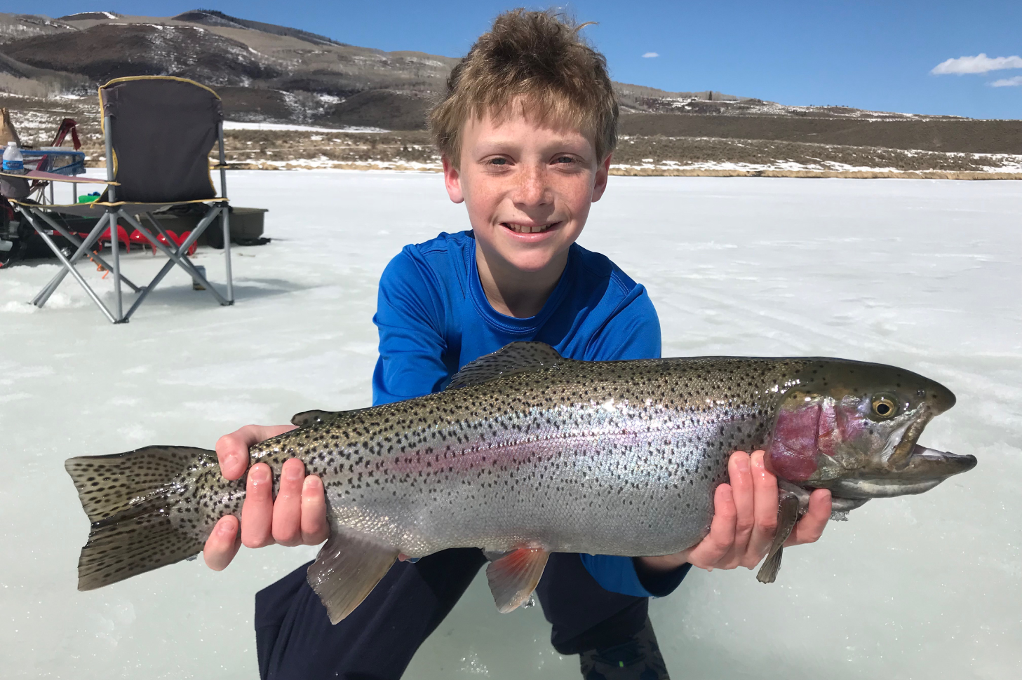 A boy holding a large fish on top of the ice.