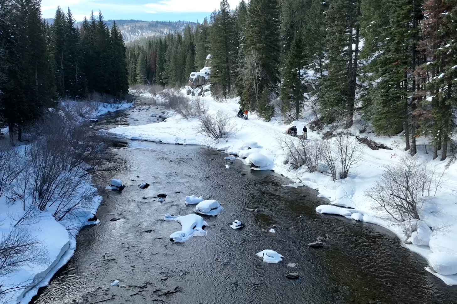 A river with snow on it and trees in the background.