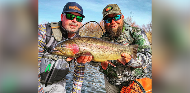 Two men holding a fish while standing in the water.