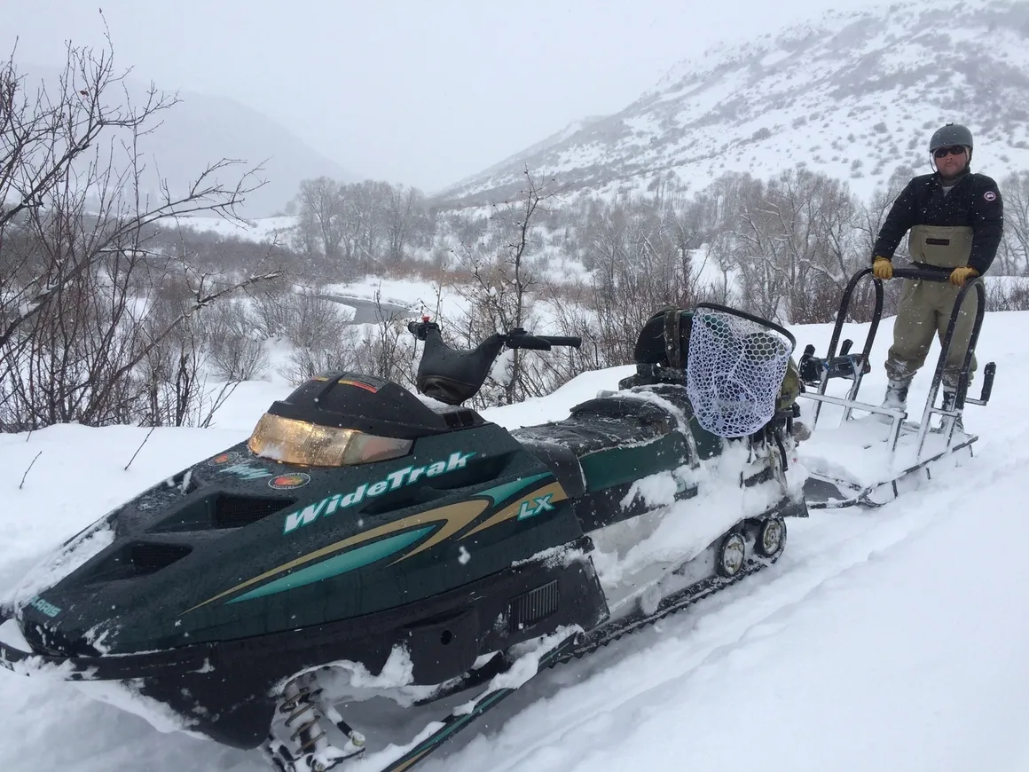 A snowmobile is parked in the snow with another vehicle.