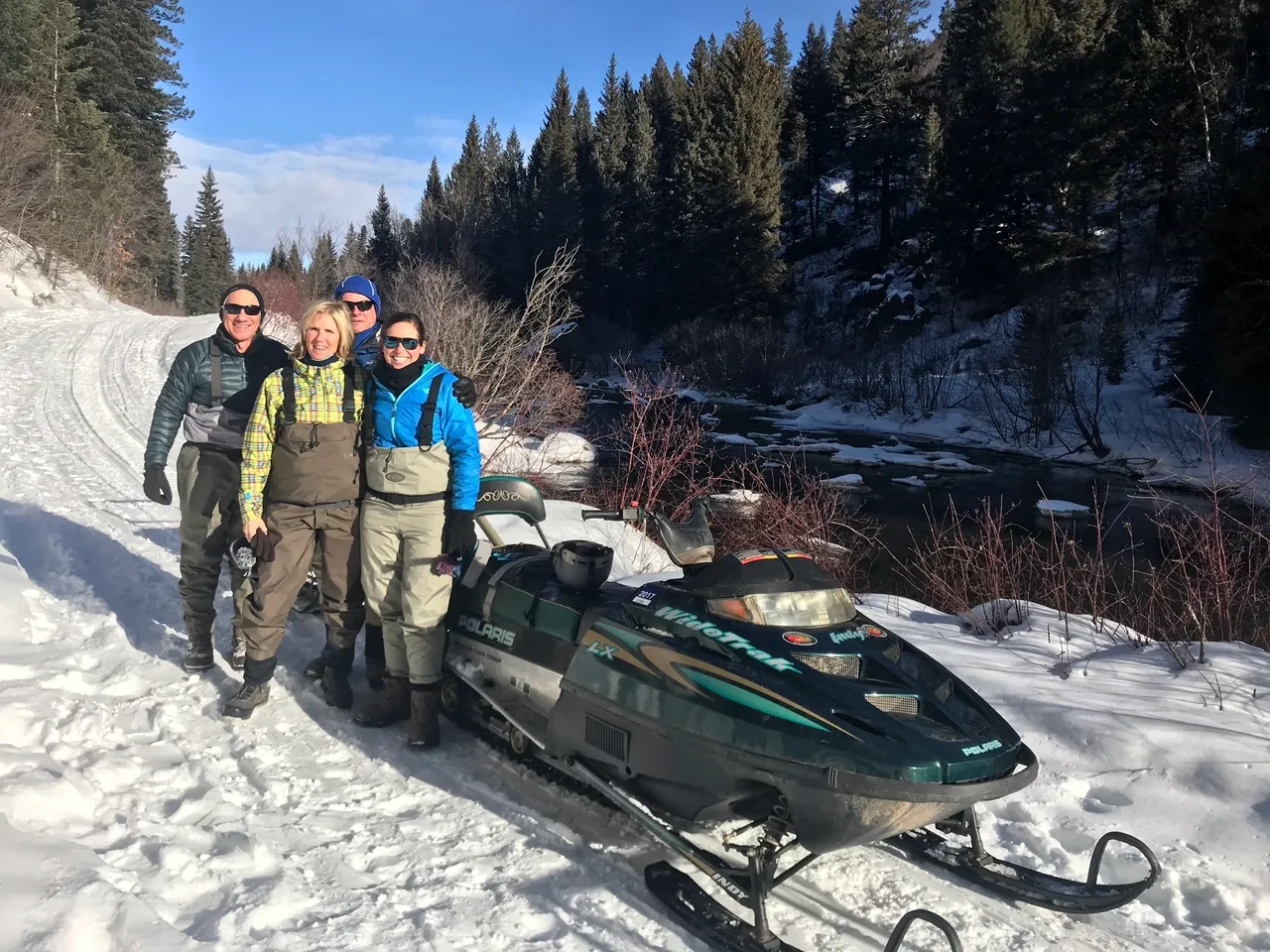 A group of people standing next to a green snowmobile.