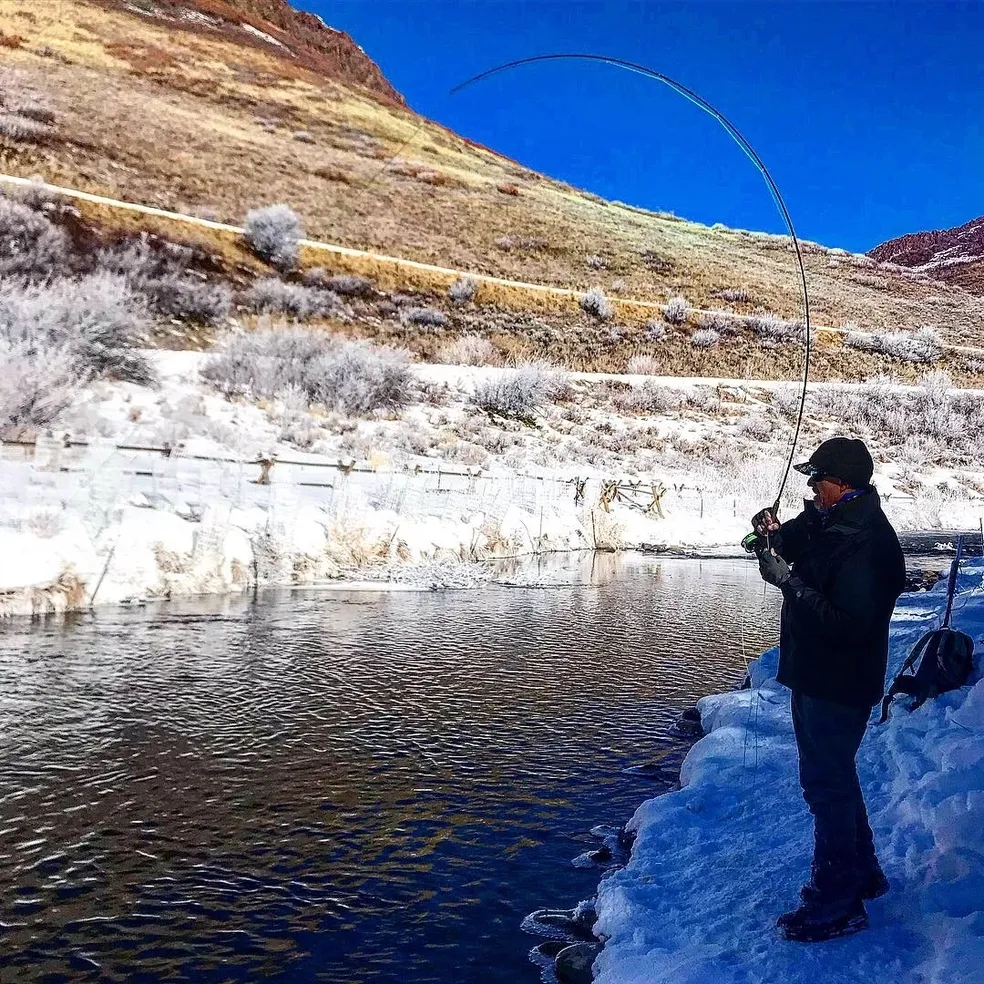 A man standing on the side of a river fishing.